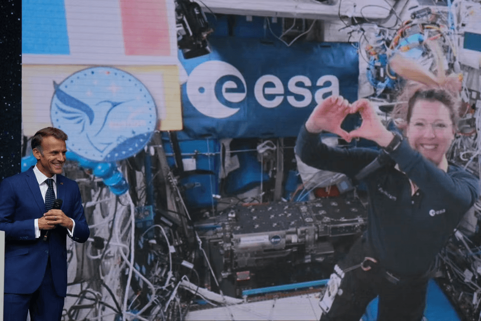 Emmanuel Macron s'exprimant sur scène devant un écran de l'ESA montrant l'astronaute française Sophie Adenot en liaison vidéo depuis la Station spatiale internationale