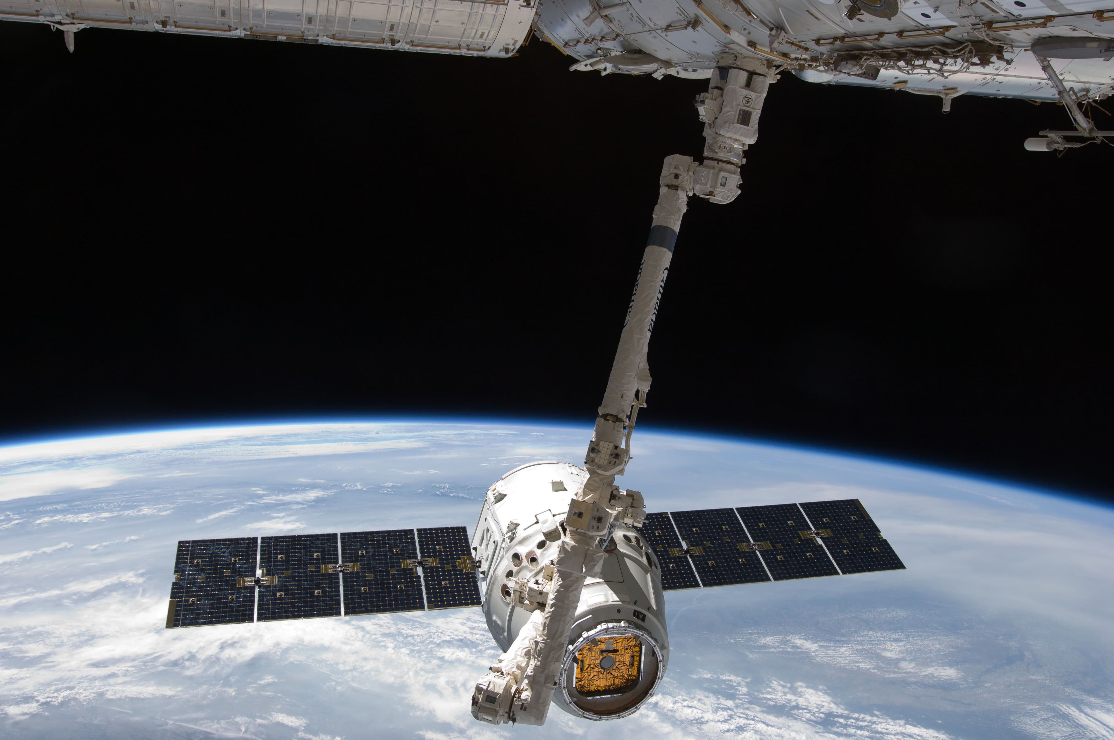 Un vaisseau cargo saisi par le bras robotique de la Station spatiale internationale, en orbite au-dessus de la Terre